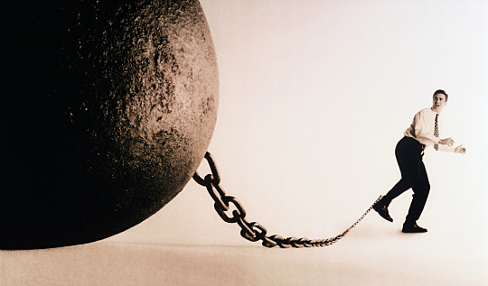 Male executive with large ball and chain attached to ankle (toned B&W)